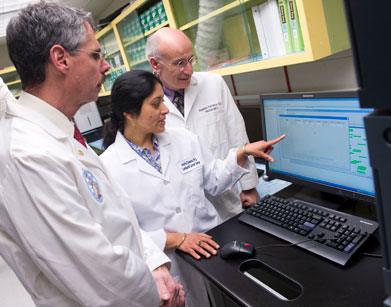 Dr. Howard J. Federoff, Amrita K. Cheema, and Dr. Massimo S. Fiandaca look at a screen in their white coats.