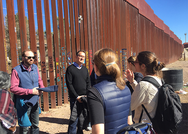 A group of six Georgetown community members stand near a fence at the U.S. border to Mexico. 