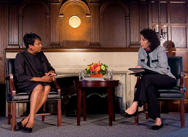 CArla Hayden and Artemis Kirk talk to one another while seated in front of a wood carved wall.