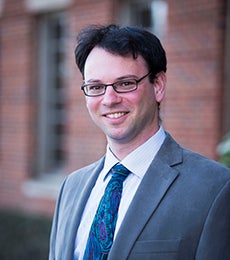 Dr. Peter Turkeltaub stands smiling with a building in the background.