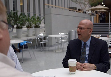 Joel Hellman, with a cup of coffee in front of him, speaks with companions at a table. 