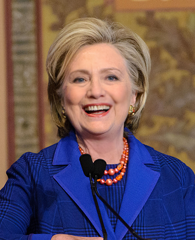 Hillary Rodham Clinton smiles while standing at the lectern.