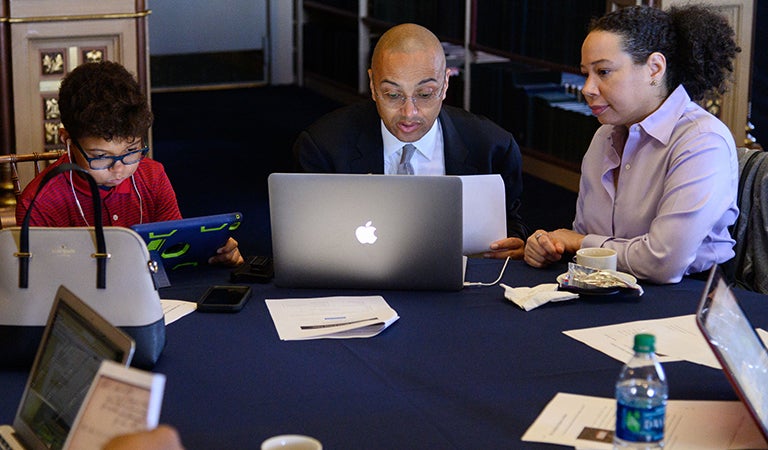 Jesse Alexander sits with his parents, Jeremy Alexander and Leslie Alexander, while they transcribe historical records on a laptop.