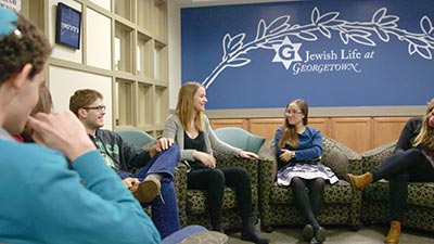 Students smile and talk beneath a painted wall that reads "Jewish Life at Georgetown."