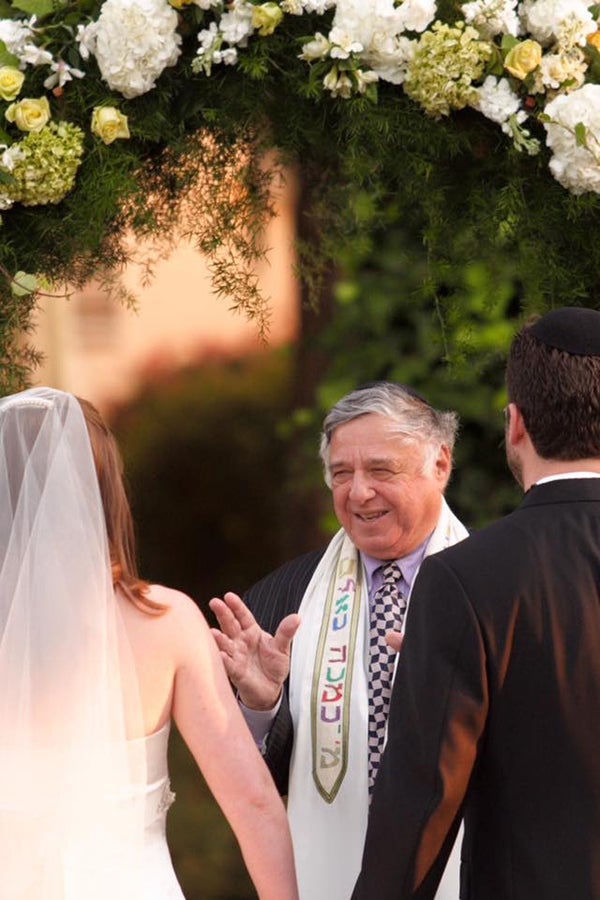 Rabbi Harold White presides over a marriage ceremony as the bride and groom stand before him.