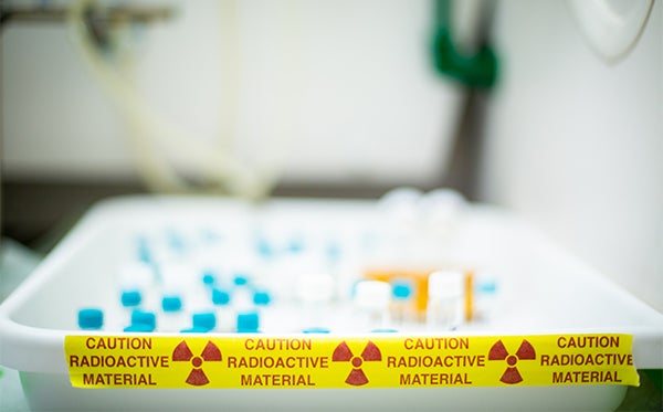 Rows of vials sit in a tray marked "Caution Radioactive Material." 