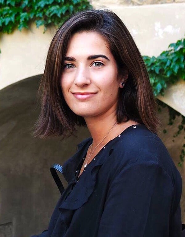 Kate Lambroza smiles wearing a navy blue shirt outside with greenery in the background.