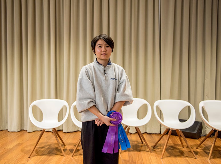 Sam Lee holding ribbons with empty white chairs and a stage curtain behind her