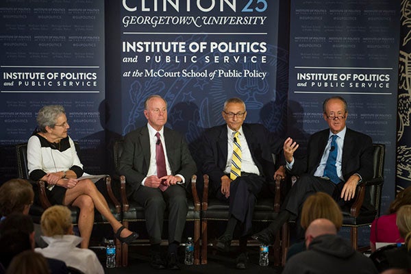 Judy Feder, Mack McLarty, John Podesta and Erskine Bowles sitting onstage with Clinton 25 banner behind them