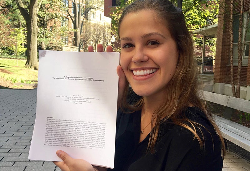 Aislinn McNiece sits on a bench outside holding a copy of her senior thesis