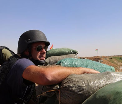 Alex Marquadt in a helmet looks out behind sandbags.