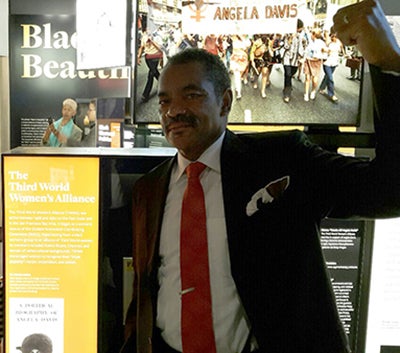 Maurice Jackson stands near a museum exhibit featuring Angela Davis with his fist in the air.