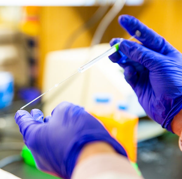 A closeup shot of hands taking a sample with a dropper in a laboratory.