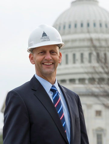 Robin Morey, in a white hard hat, smiles in front of the Capitol