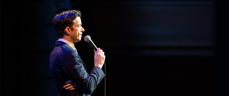 John Mulaney speaks into the microphone while on stage.