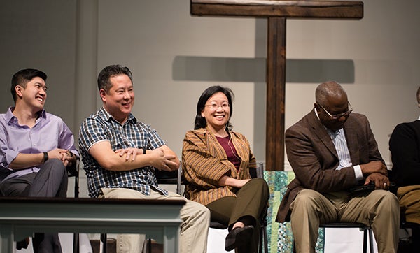 Steve Park and three other panelists sit on stage smiling at and talking to the audience in a church with a large wooden cross in the background.