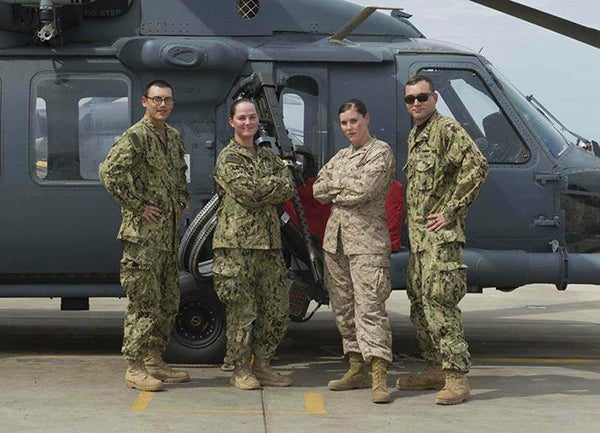 Cristine Pedersen stands in front of a helicopter dressed in camouflage with one female and two male members of her unit.