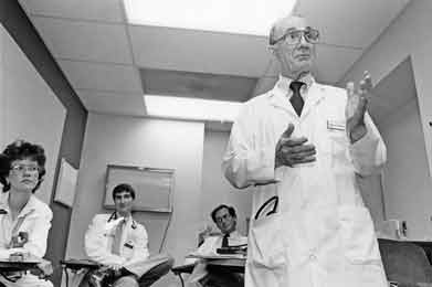 A black and white photo, taken in the 1980s, shows Dr. Edmund D. Pellegrino teaching in a classroom as students look on. 