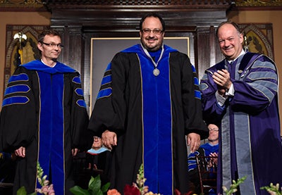 Georgetown President John J. DeGioia applauds President's Award recipients Christian Wolf and Derek Goldman onstage in Gaston Hall.