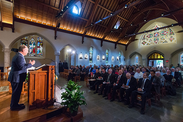 A side view from the right of Georgetown President John J. DeGioia as he speaks from behind a lectern in Dahlgren Chapel to a seated audience