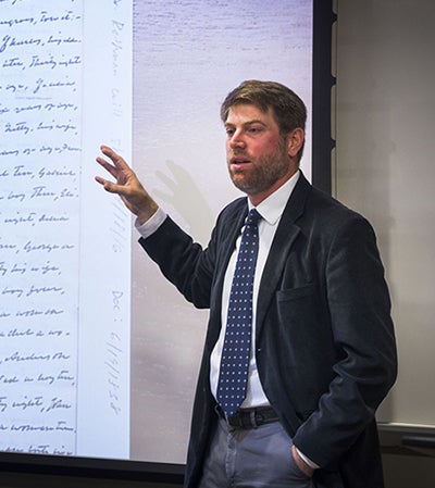 Adam Rothman standing next to screen of archival material