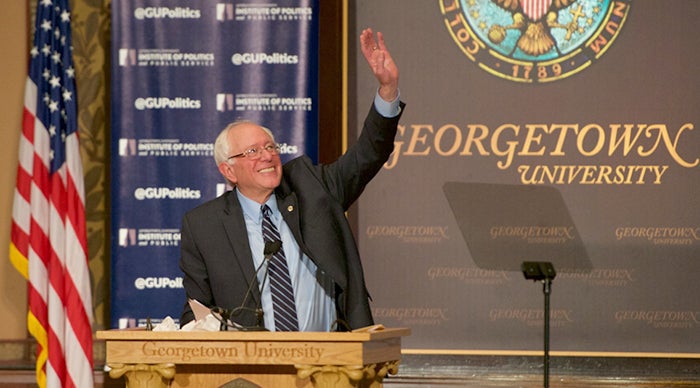 Senator Bernie Sanders smiles and waves to the crowd as he begins a speech from the podium onstage in Gaston Hall.