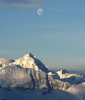 The moon sits in the sky above the ice capped formations in Antarctica 