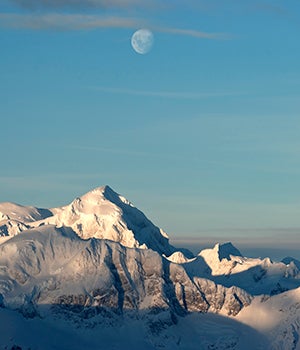 The moon sits in the sky above the ice capped formations in Antarctica 