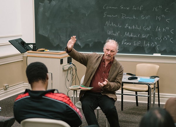 Frederick Ruf with raised hand in front of blackboard facing students in classroom 