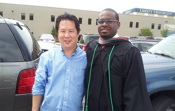 Dwaine Brown, dressed in a graduation robe, and Steve Park pose together in front of cars after Brown's graduation from Liberty University.