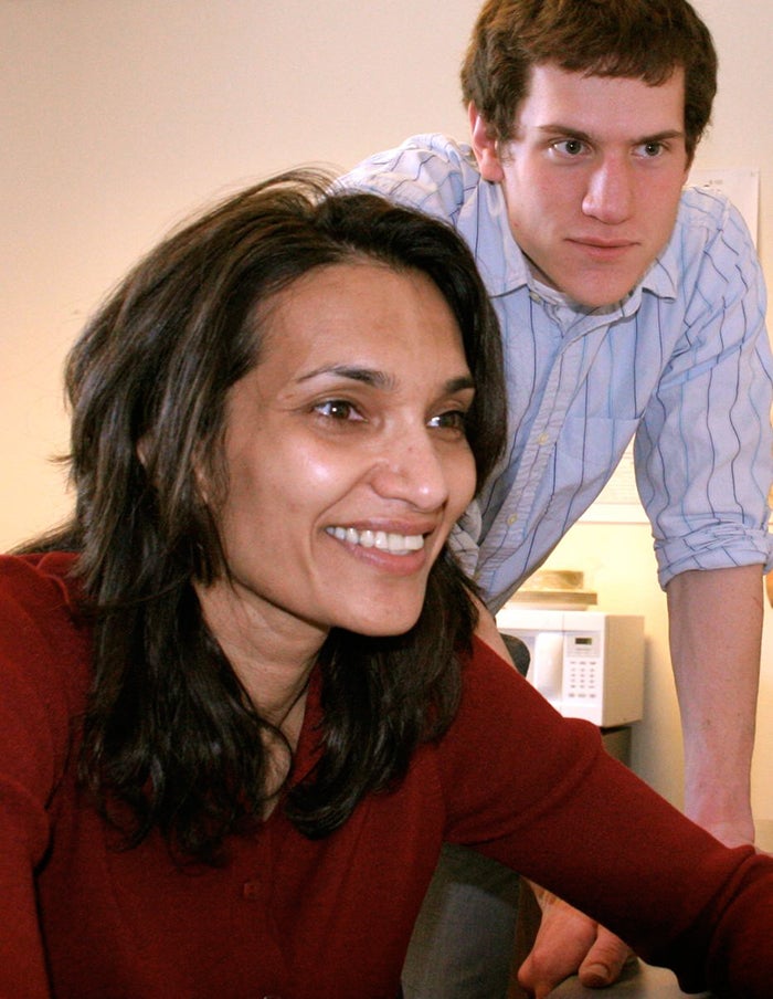 Chandan Vaidya sits at a computer reviewing material on the screen as a student stands over her listening