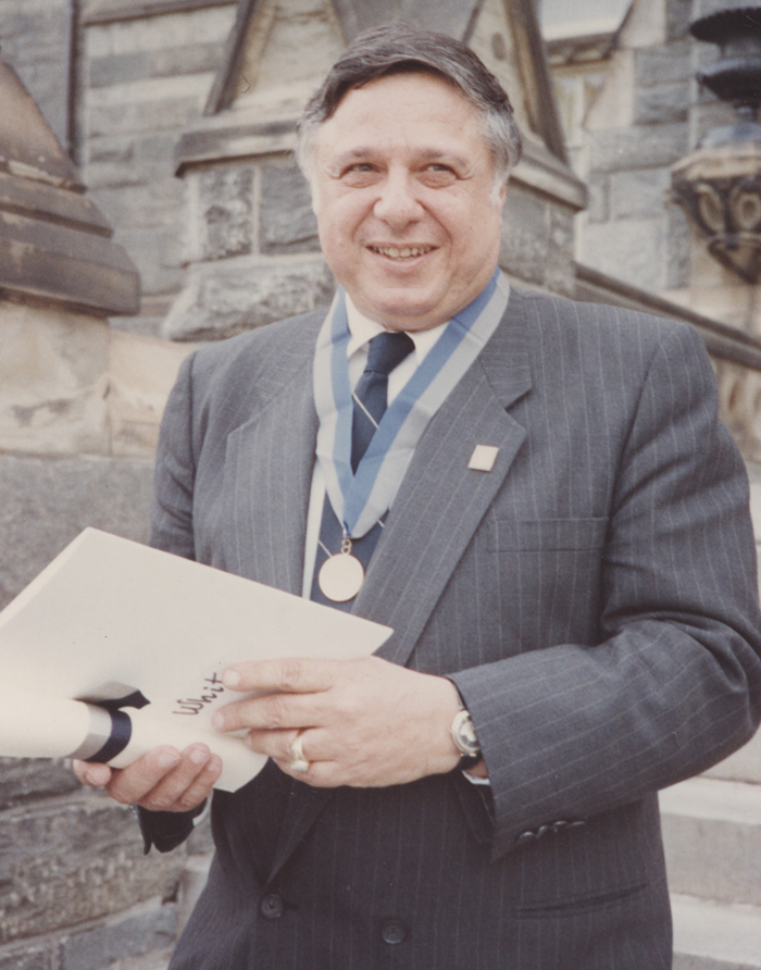 Rabbi Harold White wears medal and holds an awards as he poses for a picture on the steps of Healy Hall.