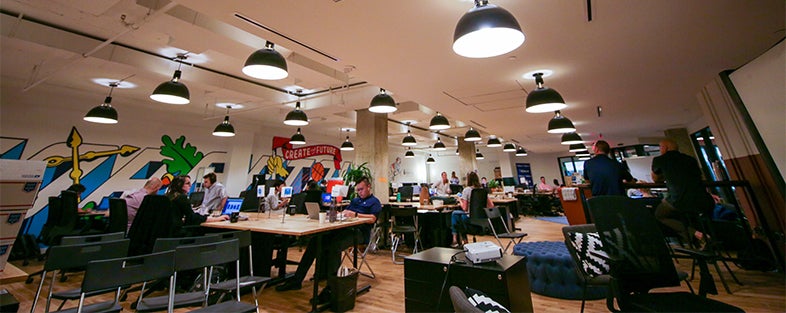 Students sit at desks working in a well-lit open space with mural art on the walls representing the Georgetown experience.