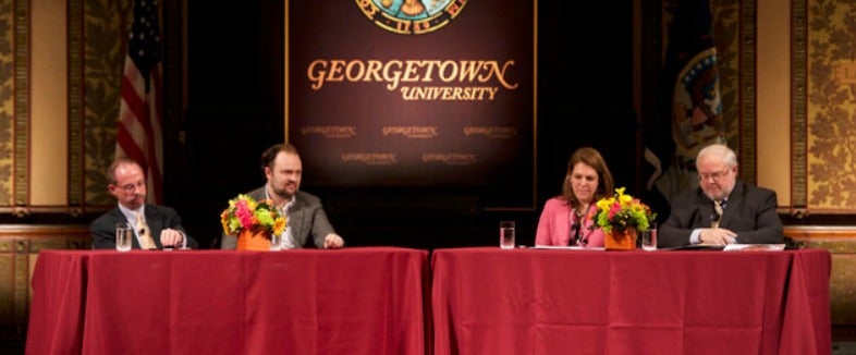 John Allen, Ross Douthat, Kerry Robinson, John Carr sit at a table with a red cloth and waters in Gaston Hall