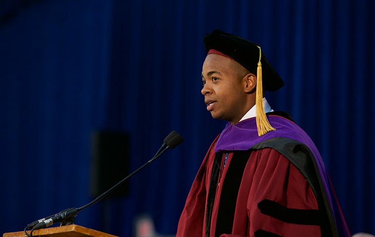 William Godwin, dressed in academic regalia, speaks to the graduating seniors of 2015