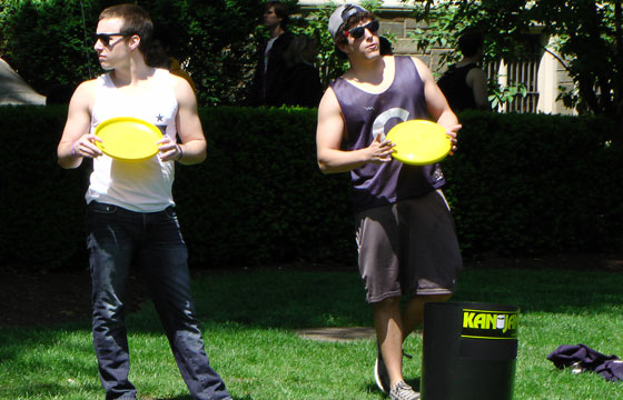 A student looks away while holding a frisbee while another tilts his head while wearing sunglasses on Copley Lawn