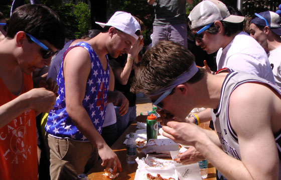Students stuff their faces with wings while standing around a table on Copley Lawn