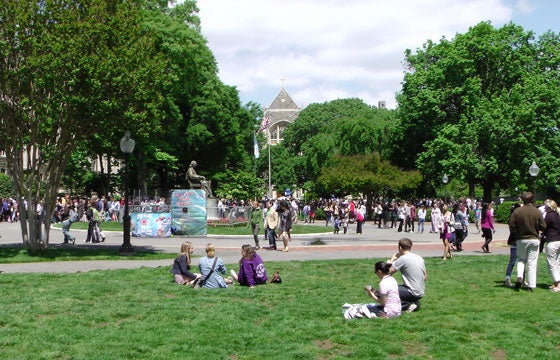 A view of Healy Lawn as students sit and stand with a dunk tank, the statue of John Carroll, trees and White Gravenor Hall 