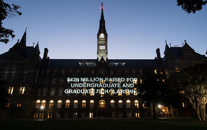 Healy Hall at Night lit up with words that read "$429 million raised for undergraduate and graduate scholarships