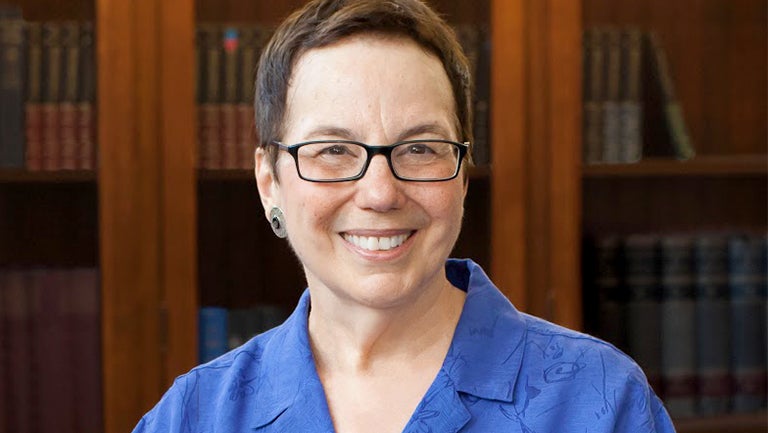 Harriette Hemmasi smiles with a wooden bookcase in the background.