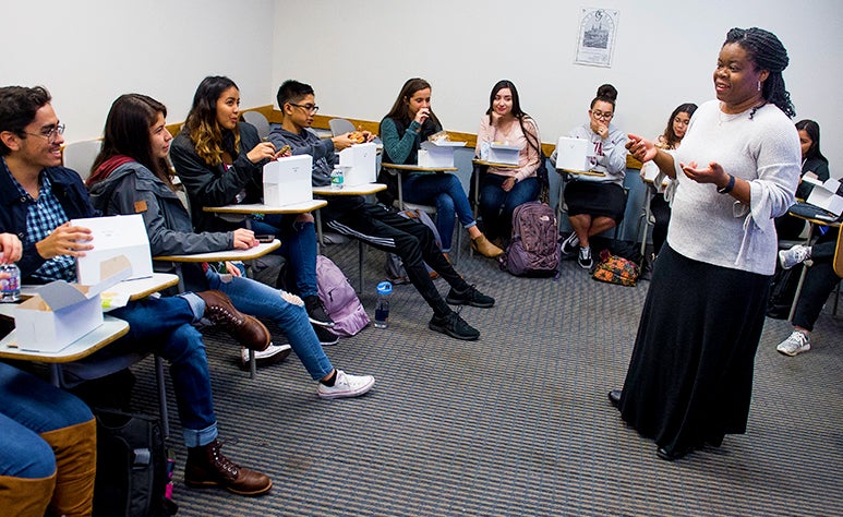 Sabrina Wesley-Nero stands in the middle of a semi circle of students sitting in desks as she teaches her course.