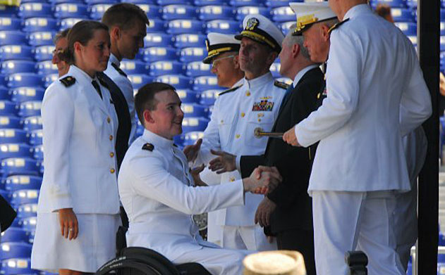 Kevin Hillery in wheelchair shakes hands with university officials at Navy commencement