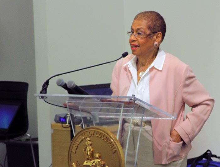 Eleanor Holmes Norton, dressed in a light pink blazer, speaks onstage during the conference