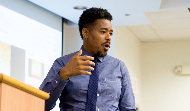 Professor Terrence Johnson delivers a lecture in a white-walled classroom as students look on.