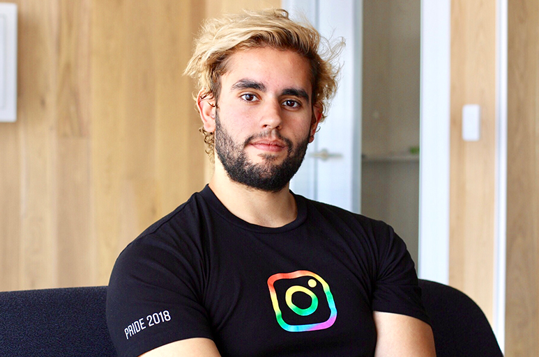 Emilio Joubert smiles into the camera in an office wearing a T-shirt with the Instagram logo on it.