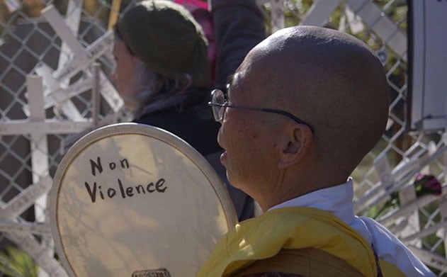 A man in crowd holds a round sign that says non violence