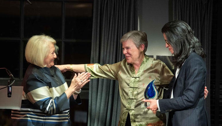 Melanne Verveer claps as Rose Gottemoeller extends her arm and Shéhérazade Semsar-de Boisséson presents the award