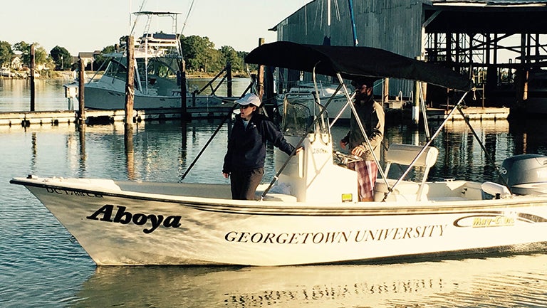 Researchers stand aboard a boat named Ahoya while docking on the river.