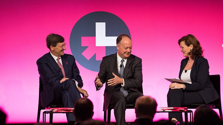 Vittorio Colao, John J. DeGioia and Susanna Schrobsdorff sit on chairs with he for she logo banner behind them