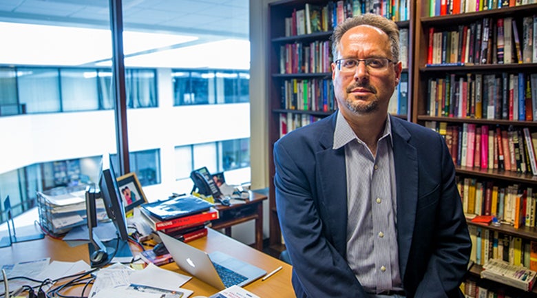 Professor Michael David-Fox sitting on the edge of his desk in his office